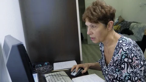 Elderly woman at the computer sits at a table in the home office Stock Footage 123311709