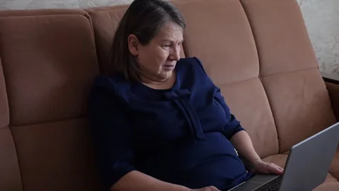 Elderly woman crying while using laptop on sofa Stock Footage 311483697