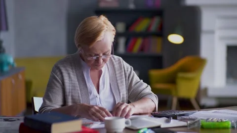 An elderly woman, deeply focused, is working diligently at her home office desk Stock Footage 293461759