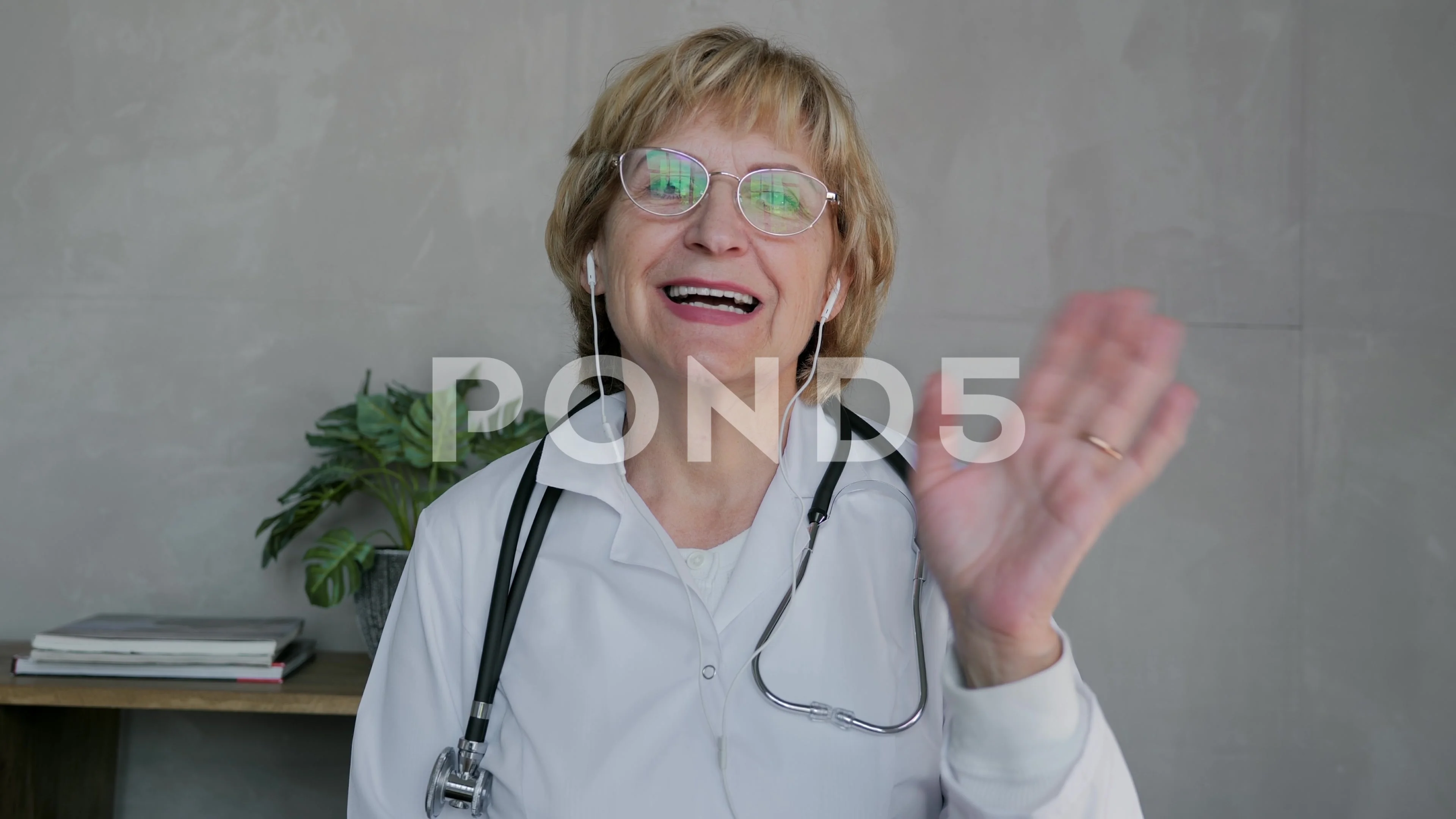 An elderly woman doctor speaks on a video call and looks into the camera