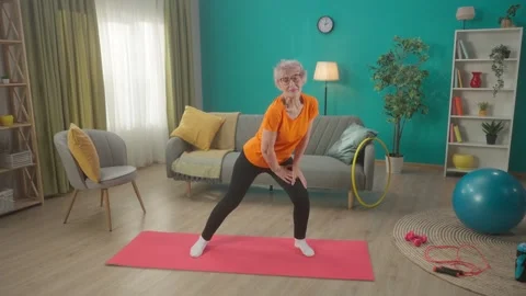 Elderly woman doing side lunges while exercising. A grayhaired retired woman Stock Footage 245408745