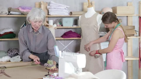 Elderly woman drawing pattern on paper female assistant sews on mannequin Stock Footage 327695796
