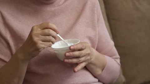 Elderly Woman Eats Yogurt While Sitting on a Couch 스톡 동영상 278183208