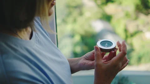 Elderly woman holding a compass while looking out of a window in a quiet room du Stock Footage 331283145
