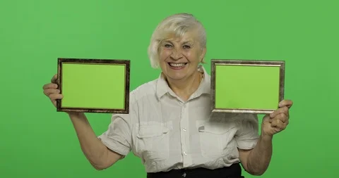 An elderly woman holding two frames with green image. Grandmother. Chroma key Stock Footage 113097630