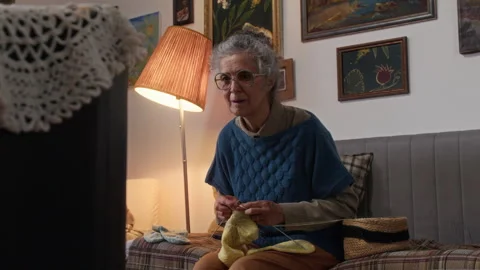 Elderly Woman Knitting on Sofa While Watching TV in her Cozy Living Room Stock Footage 314622509