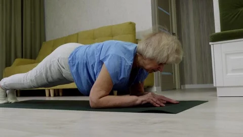 Elderly woman practicing plank exercise on yoga mat at home Stock Footage 313252034
