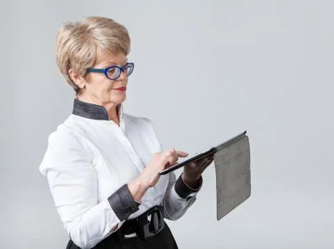 Elderly woman presses a touchscreen tablet, gray background Foto stock