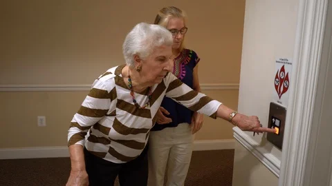 Elderly woman pushes an elevator button while pretty woman in ethnic Stock Footage 117130879