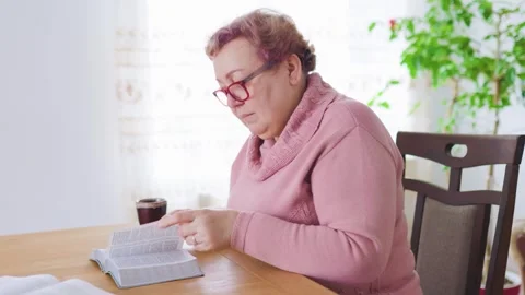 Elderly woman reading a book while enjoying a quiet morning indoors Stock Footage 305162670