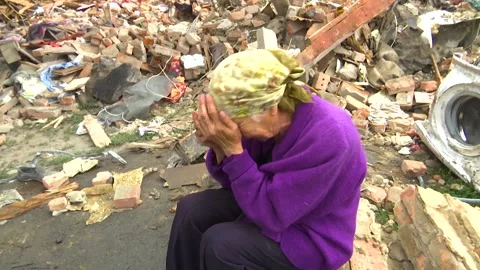 An elderly woman sits and cries on the ruins of her house after a missile strike Stock Footage
