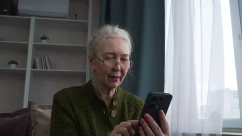 Elderly woman smiling while using a smartphone on the couch Stock Footage 304779554