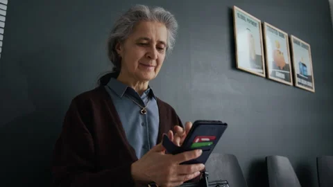Elderly Woman Smiling While Using Smartphone in Waiting Room of Bank Office Stock Footage 310117640