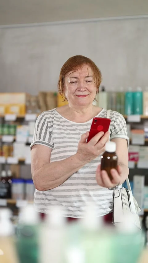 Elderly woman in summer clothes scans code on cough syrup to check the Stock Footage 320446853