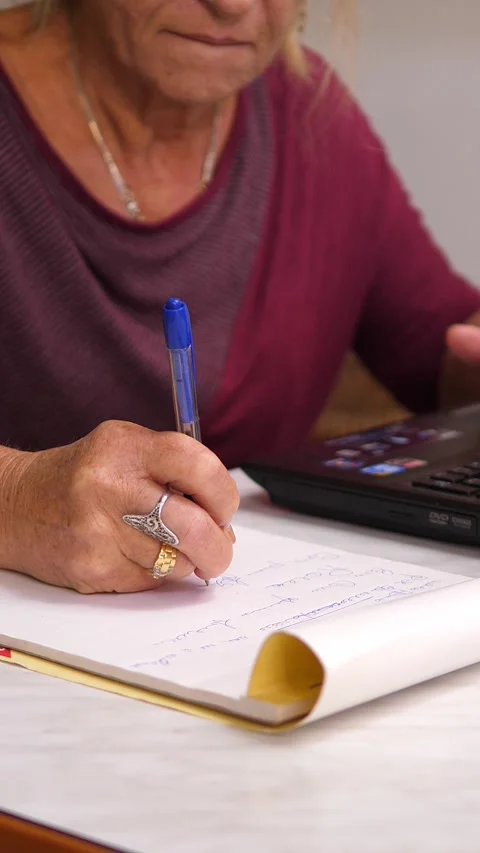 Elderly woman taking notes while working on laptop Stock Footage 320254808