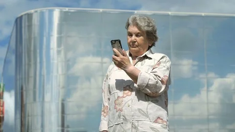Elderly woman talks using a smart phone outdoors Stock Footage 79468994