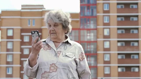 Elderly woman talks using a smart phone outdoors Stock Footage 79471308