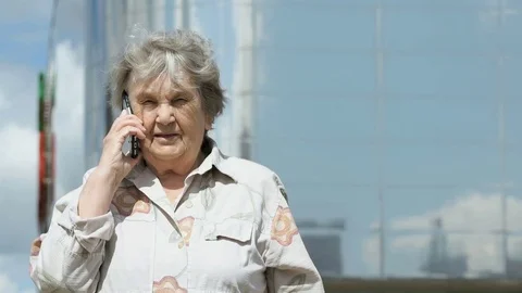 Elderly woman talks using a smart phone outdoors Vídeo Stock 80368661
