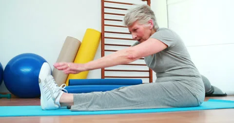Elderly woman touching her toes on exercise mat Stock Footage