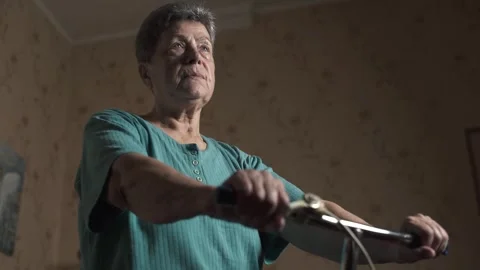 Elderly woman training on a retro exercise bike in a modest room. Montage. Stock-Footage 288508002