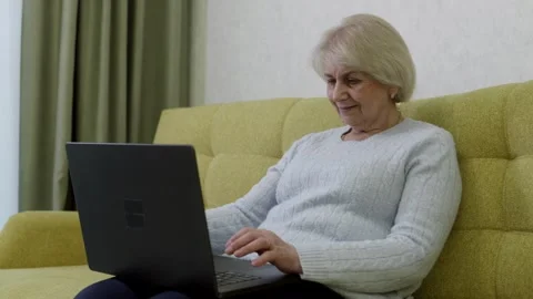Elderly woman using laptop computer on sofa Video stock 313512425