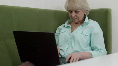 Elderly woman using laptop computer on green sofa Stock Footage 321856189