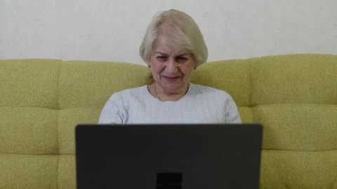 Elderly woman using laptop while sitting on sofa Stock Footage 321855888