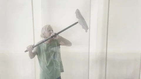 Elderly woman using a long-handled squeegee mop to clean a high glass window Video stock 333990136