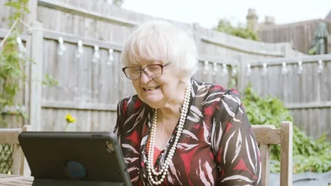 Elderly Woman using skype waves to tablet device, laughs and speaks in garden Stock Footage