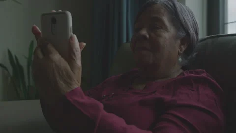 Elderly woman using smartphone while seated in cozy home setting Stock Footage 312625177