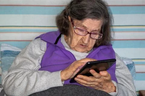 Elderly woman using a tablet in bed, focused on reading and navigating the Stock Photos