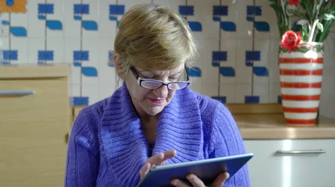 Elderly woman using tablet computer in the kitchen: facebook, twitter, mail, web Video stock 47859081