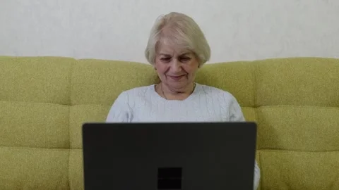Elderly woman using tablet device on green sofa with focused concentration Vidéo 322812024