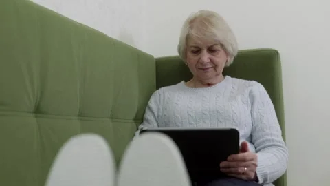 Elderly woman using tablet while relaxing on sofa Stock Footage 321855950