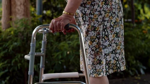 Elderly Woman Using Walker for Support in Outdoor Garden Stock Footage 332636660