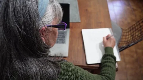 Elderly woman writing in notepad during online study session Video stock 346326470