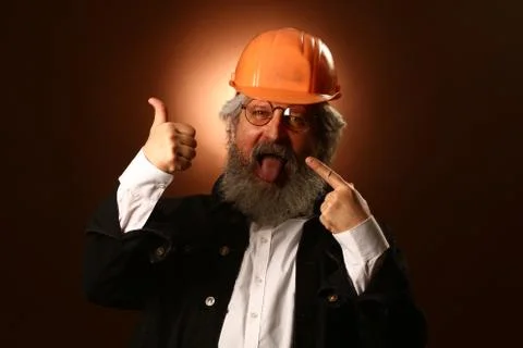 An elderly worker in a helmet gestures warning signs, studio portrait Foto stock