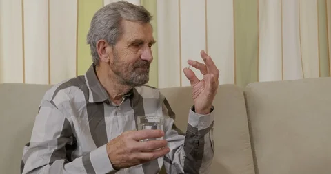 Eldery man with grey beard takes pill and drinks water from glass for health Stock Footage 130026646