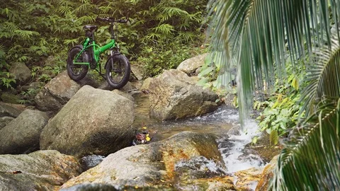 Electric Bicycle Parked on Rocks over Tropical Mountain Stream 스톡 동영상 82443323