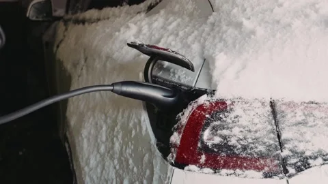 Electric car charging cable plugged into snowy vehicle port outdoors Stock Footage 329850608