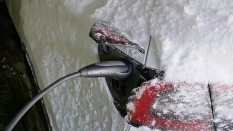 Electric car charging cable plugged into port on snowy vehicle in winter Stock Footage 329913758