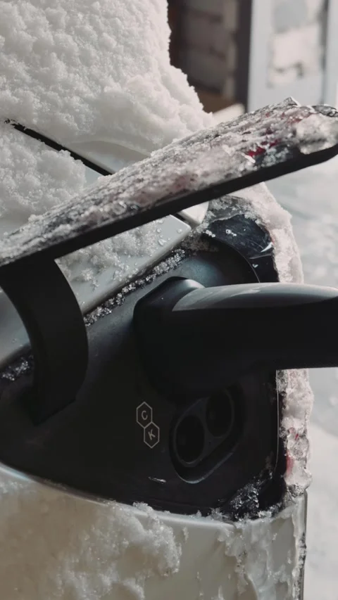 Electric car charging cable plugged into vehicle covered in snow during winter Stock Footage 329963238