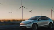 An Electric Car Drives Along The Road Against The Backdrop Of Wind Power Plants Stock Footage