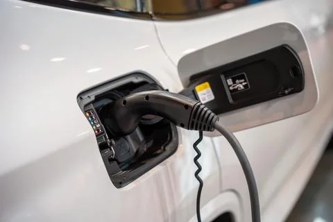 Electric car (EV) is charging in socket with cable. Stock Photos