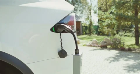 A electric car with a power cable connected to a charger stands in the backyard Stock Footage 163978029