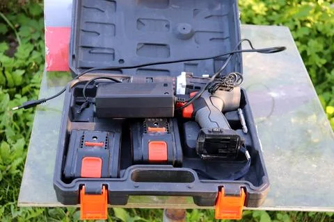 Electric drill in plastic open box, suitcase on glass table in garden Stock Photos