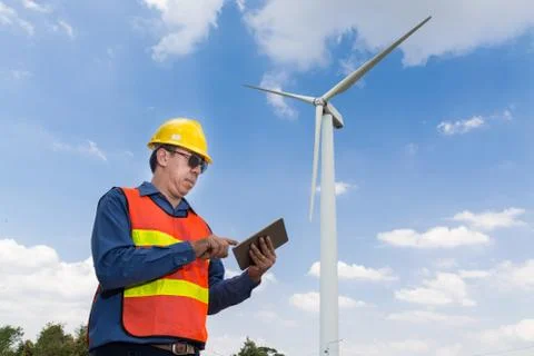 Electric Engineer use Tablet Device with Wind turbine power Generator Tower Stock Photos