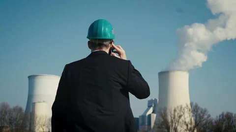 Electric engineer wearing helmet and suit in front of coal fired power station Stock Footage 209298182