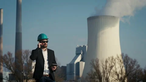 Electric engineer wearing helmet and suit in front of coal fired power station Stock Footage 209343982