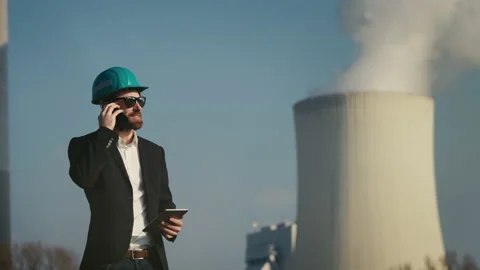 Electric engineer wearing helmet and suit in front of coal fired power station Stock Footage 209345951